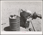Syphoning gas from storage container to use in truck-tractor. Pie Town, New Mexico