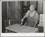 Mrs. George Hutton brushing on paste on wall paper which her son is hanging for her. Pie Town, New Mexico