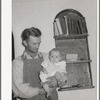 Mormon farmer with his baby in front of a bookshelf in his home. Snowville, Utah