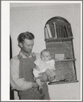 Mormon farmer with his baby in front of a bookshelf in his home. Snowville, Utah