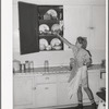 Daughter of Mormon farmer putting away dishes in kitchen cabinet. Box Elder County, Utah