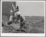 Mixing plaster for house, Chamisal, New Mexico. Occasionally a man helps with the hard work of mixing plaster but the women never allow the men to help with the actual plastering of the house