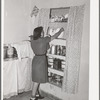 Daughter of Spanish-American putting dishes into cupboard. Chamisal, New Mexico