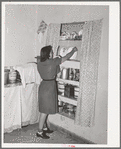 Daughter of Spanish-American putting dishes into cupboard. Chamisal, New Mexico