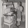 Spanish-American woman stirring pan of cooking beans. Small boy is roasting sweet corn on top of the stove. Chamisal, New Mexico