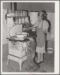 Spanish-American woman stirring pan of cooking beans. Small boy is roasting sweet corn on top of the stove. Chamisal, New Mexico