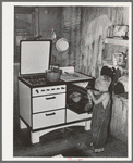 This workman's son is taking gingerbread out of kitchen stove which cost his father one hundred thirty-five dollars and he lives in a shack-house in the Mexican section of town because the father couldn't find anything better for the family