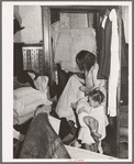 Corner of bedroom with Negro housewife examining bed clothing chewed by rats. Chicago, Illinois