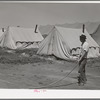 Farm worker watering down the dusty ground around his tent at the FSA (Farm Security Administration) migratory labor camp mobile unit. Wilder, Idaho