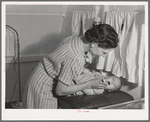 Nurse at the FSA (Farm Security Administration) migratory labor camp mobile unit, examines throat of baby in trailer-clinic. Wilder, Idaho