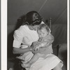 Nurse looks at cut on baby's arm at the FSA (Farm Security Administration) migratory labor camp mobile unit. Wilder, Idaho. The nurse not only is in attendance at the trailer clinic, but makes her regular rounds of calls to the tents