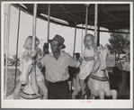 Father with his two daughters on the merry-go-round, one of the carnival attractions at the Fourth of July celebrations