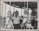 Father with his two daughters on the merry-go-round, one of the carnival attractions at the Fourth of July celebrations