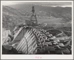 Shasta Dam under construction. Cable cars carrying materials operate from the high tower. Shasta County, California