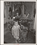 Child of agricultural day laborer in front of dressing table in shack. Near Vian, Oklahoma