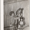 Migrant boy removing guitar before they leave for California. At old homestead near Muskogee, Okla