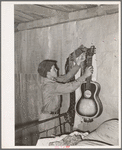 Migrant boy removing guitar before they leave for California. At old homestead near Muskogee, Okla