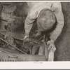 Migrant boy who is somewhat of a mechanic checking up the lighting wires of their improvised truck which will carry them to California. Near Muskogee, Oklahoma