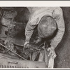 Migrant boy who is somewhat of a mechanic checking up the lighting wires of their improvised truck which will carry them to California. Near Muskogee, Oklahoma