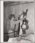 Migrant boy removing guitar before they leave for California. At old homestead near Muskogee, Oklahoma
