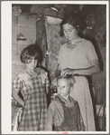 Woman in shack home in community camp. Oklahoma City, Oklahoma. Straightening her son's hair