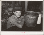 Boy sitting at table in his shack home near Mays Avenue camp. Oklahoma City, Oklahoma