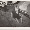 Child of large family sitting on bedding in shack home. Mays Avenue camp, Oklahoma City, Oklahoma