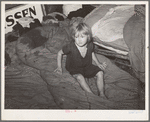 Child of large family sitting on bedding in shack home. Mays Avenue camp, Oklahoma City, Oklahoma