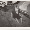 Child of large family sitting on bedding in shack home. Mays Avenue camp, Oklahoma City, Oklahoma