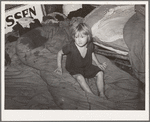 Child of large family sitting on bedding in shack home. Mays Avenue camp, Oklahoma City, Oklahoma
