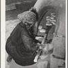 Spanish-American woman removing baked bread from outdoor earthen oven by means of a long wooden paddle. Near Taos, New Mexico