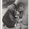 Spanish-American woman removing baked bread from outdoor earthen oven by means of a long wooden paddle. Near Taos, New Mexico