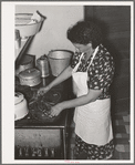 Spanish-American woman placing and turning peppers on the stove near Taos, New Mexico