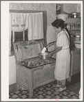 Spanish-American woman taking flour from old-type flour bin in her home near Taos, New Mexico