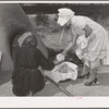 Wiping ashes from freshly-baked bread which has just been removed from earthen oven. Spanish-American farm home near Taos, New Mexico