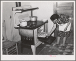 Spanish-American woman removing baked bread from oven farm near Taos, New Mexico