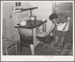 Spanish-American woman removing baked bread from oven farm near Taos, New Mexico