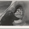 Spanish-American woman putting boards over entrance of outdoor oven to retain heat for baking bread. Near Taos, New Mexico