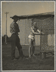 Ted Shawn standing with man outdoors and washing hands under water tap with bucket
