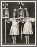 Unidentified showgirls [with cockatiels in pole-mounted cages] in the stage production Jumbo