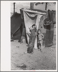 Two children of a migrant fruit worker from Tennessee, standing before their temporary home. This family of eight is camped in a field near the packinghouse at Winter Haven, Florida