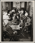 Women playing cards at various tables in the parlour 