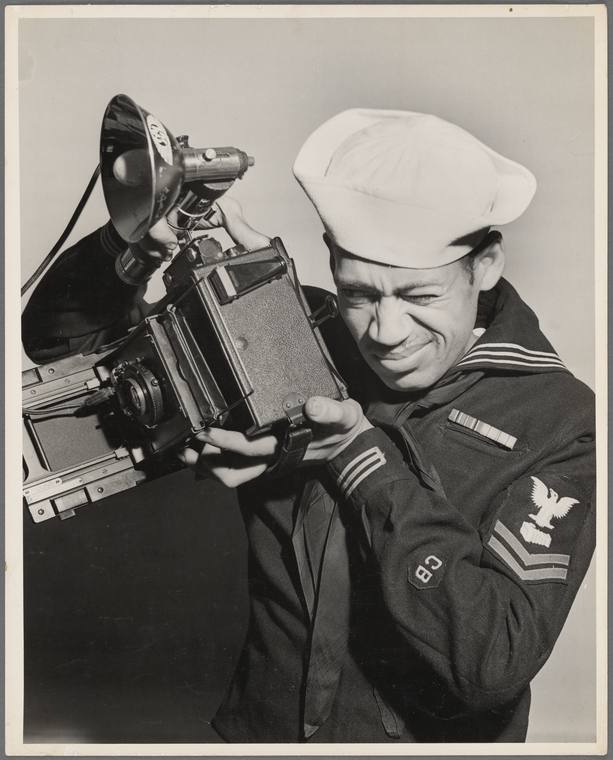 Portrait of Austin Hansen in naval uniform with a Speed-Graphic camera