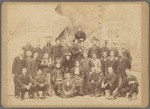 Group shot in front of Folies Bergère poster with Loie Fuller and large group of men 