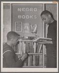 Two U.S. Navy sailors browsing library shelf labeled "Negro Books"