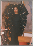 Model in Patrick Kelly Paris fashion show, wearing black dress and holding up part of garment with gold embellishments