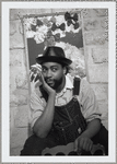 Patrick Kelly, wearing a leather hat and overalls, poses in front of a mixed-media painting