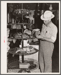 Farmer examines brushes for horses, cattle and hogs. Harness shop, Grundy Center, Iowa