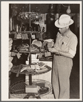 Farmer examines brushes for horses, cattle and hogs. Harness shop, Grundy Center, Iowa