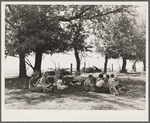 Teacher eats lunch with children in shade of trees on school grounds. Grundy County, Iowa